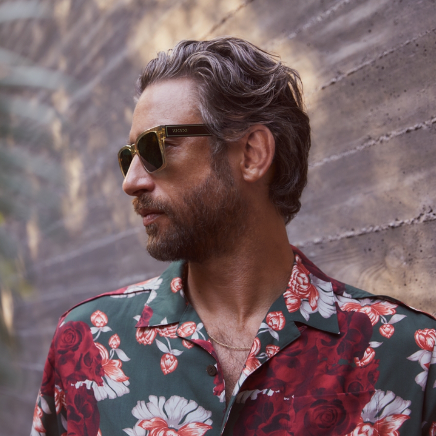 Man wearing dark sunglasses with the brand name "WAWAY" on the temple, floral shirt, and gold chain.