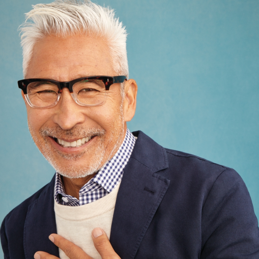 Smiling man wearing black glasses, a blue blazer, and a checkered shirt.