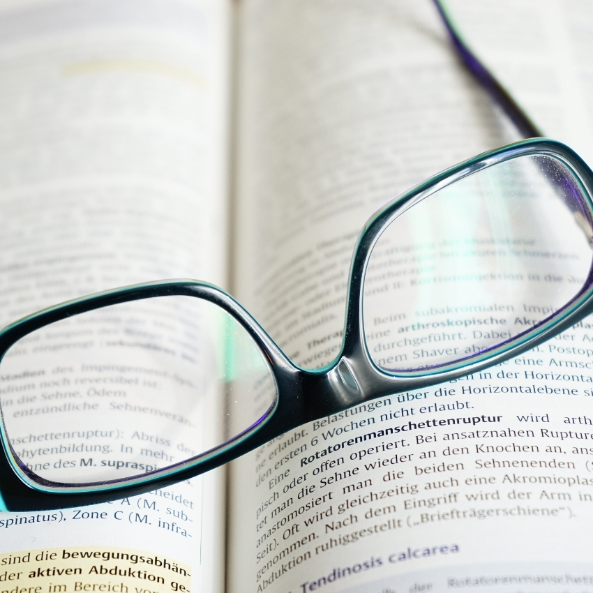 Eyeglasses resting on an open book displaying text in German.