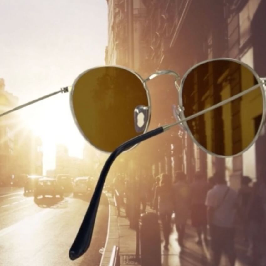 Round sunglasses with gold frames and brown lenses against a sunlight backdrop.