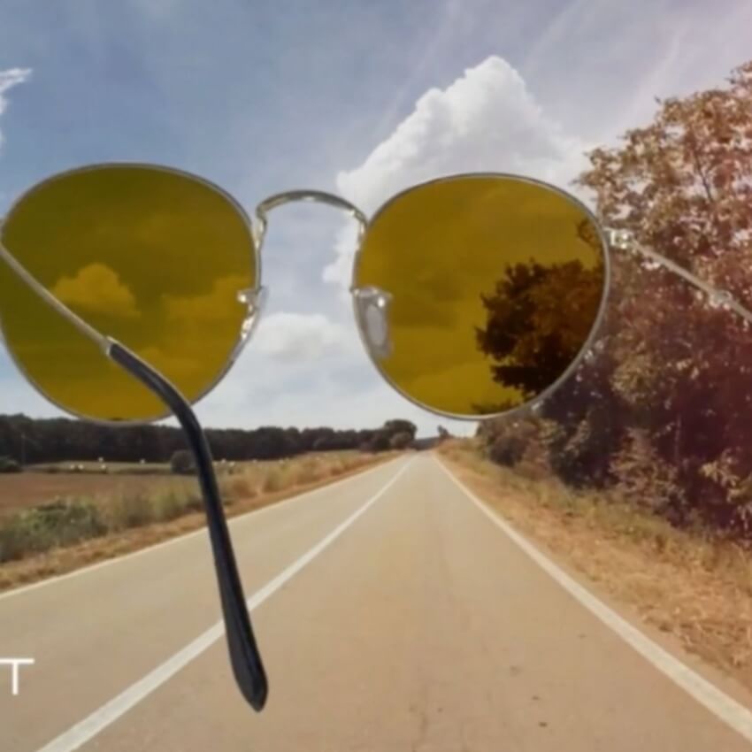 Yellow-tinted round sunglasses held up against a country road backdrop.