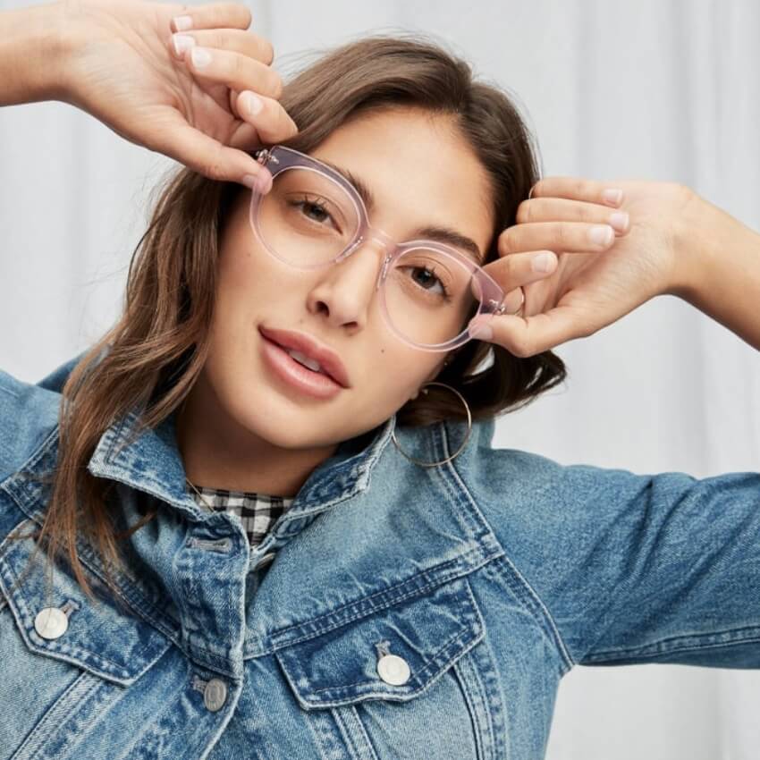 Woman wearing clear pink round glasses and a denim jacket.