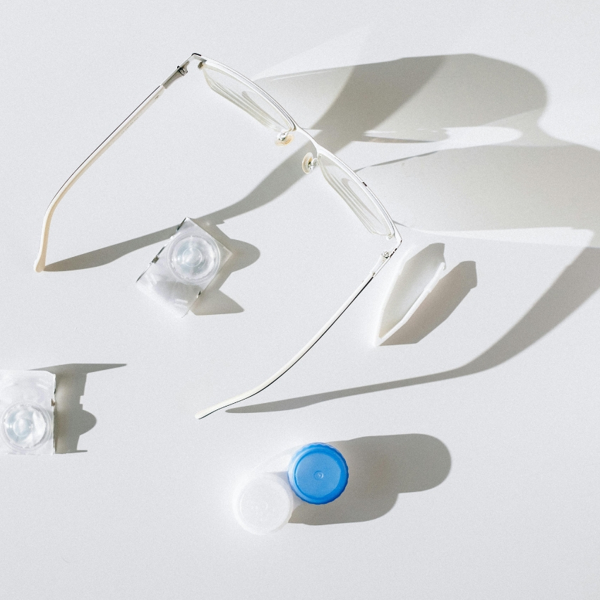 Glasses frame, contact lens blister packs, and a blue and white contact lens case on a white surface.