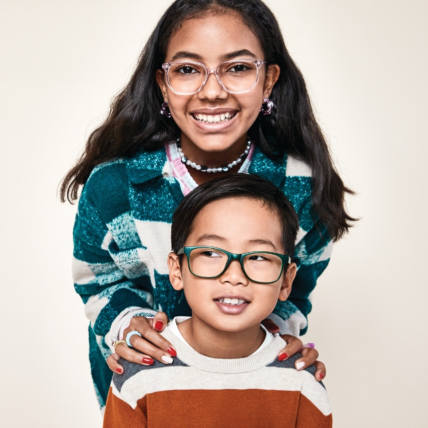 Children wearing stylish eyeglasses; girl in clear frames and boy in green frames.