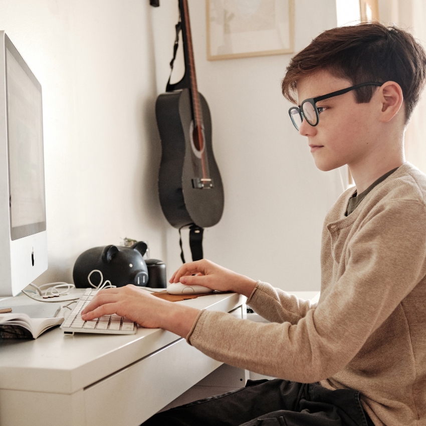 Young person using an Apple iMac at a white desk.