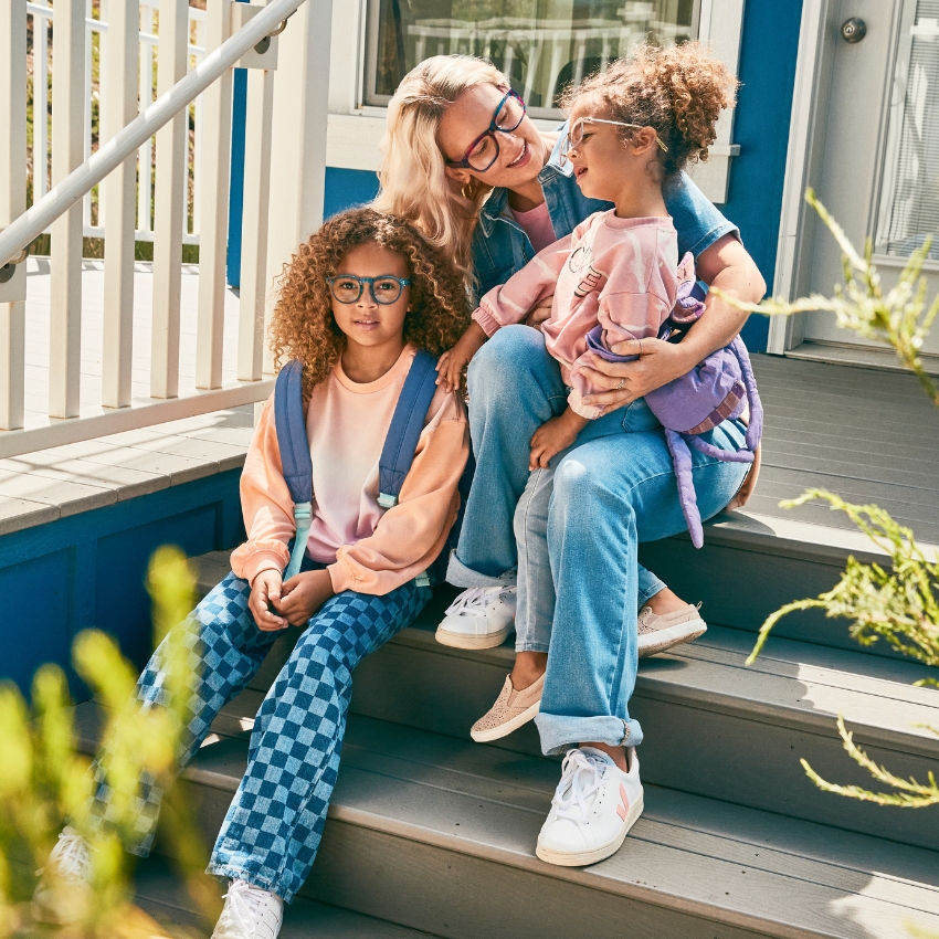 Three individuals wearing stylish eyeglasses, seated on outdoor steps, showcasing trendy casual outfits.