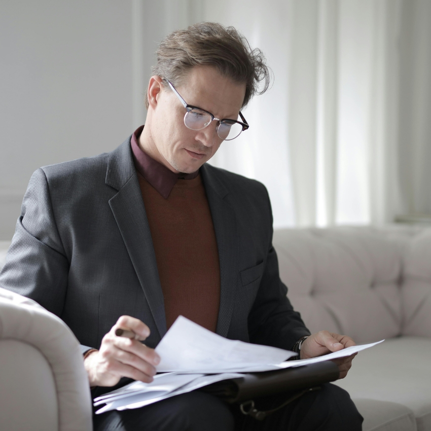 Man in suit reviewing documents with pen in hand.