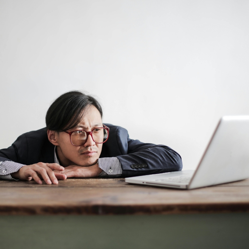 Man with red glasses looking at an open laptop on a wooden table.