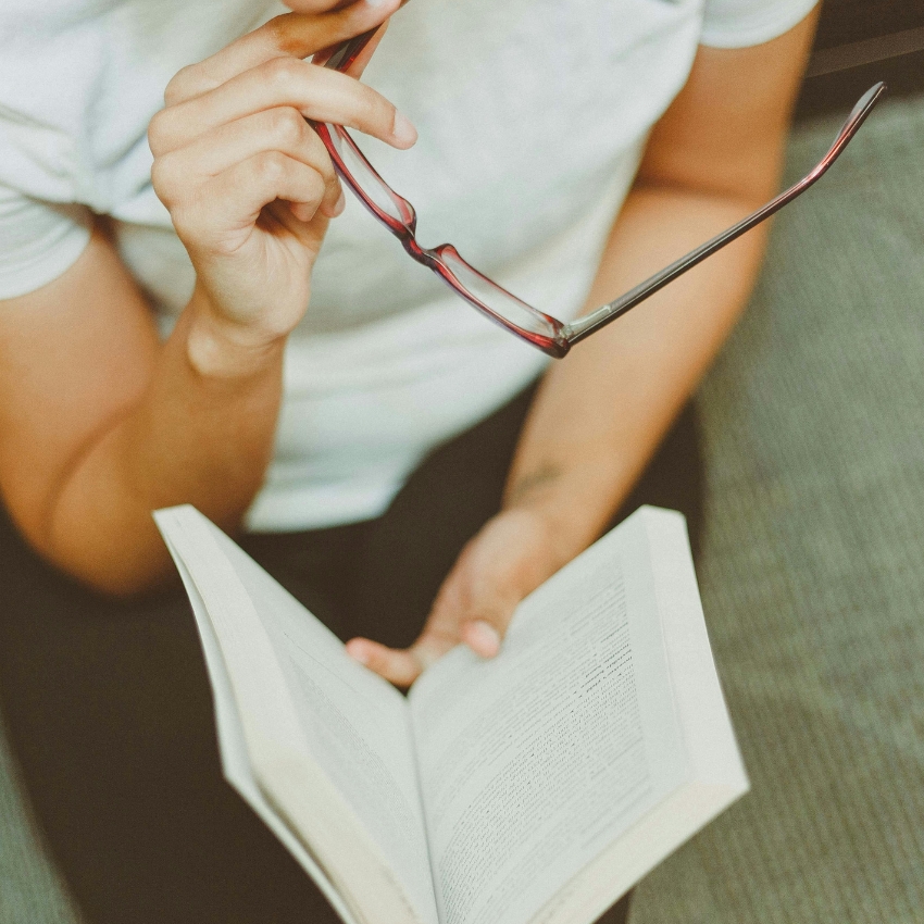 Person holding red glasses, reading an open book.