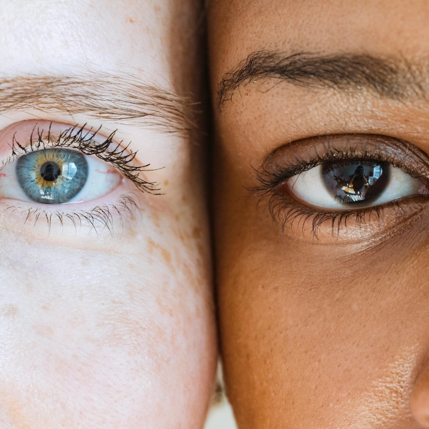 Close-up of two eyes: blue and brown, with different skin tones highlighting diversity.