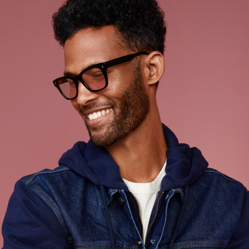 Man wearing black-framed eyeglasses, a navy hoodie, and a denim jacket.