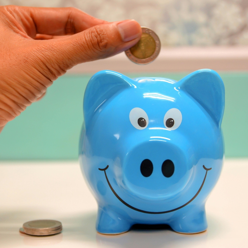 Hand placing a coin into a smiling blue piggy bank.