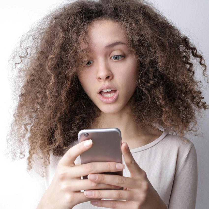 Woman holding a smartphone, looking surprised.