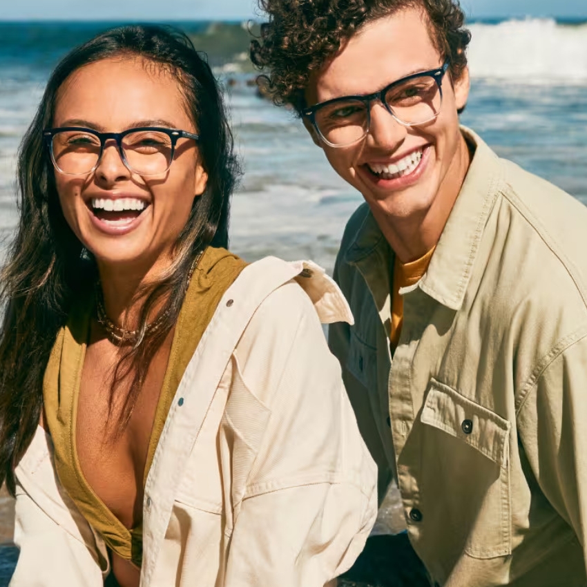 Two people smiling and wearing black-framed eyeglasses on a sunny day.