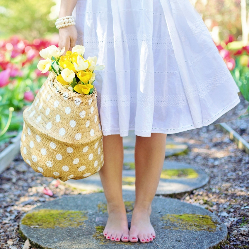 Wicker basket with white polka dots, filled with yellow flowers, held by a person wearing a white dress.