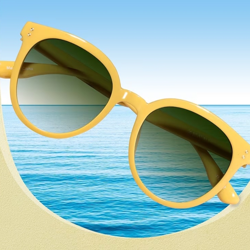 Yellow round sunglasses with green-tinted lenses, beach and ocean in background.