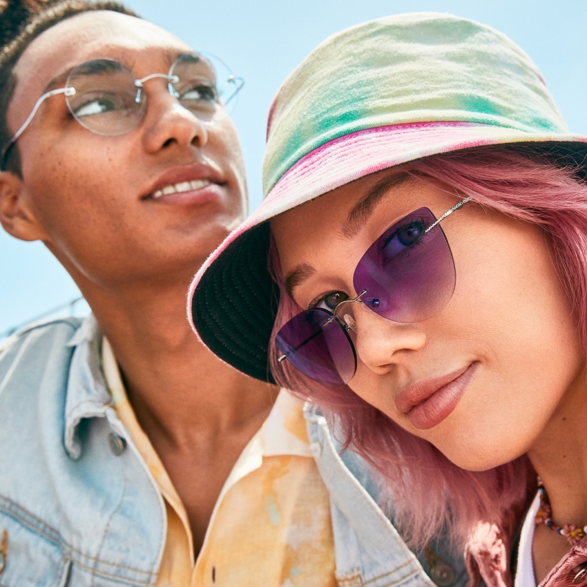 Person wearing purple sunglasses and a multicolored bucket hat. Another person wearing clear glasses.