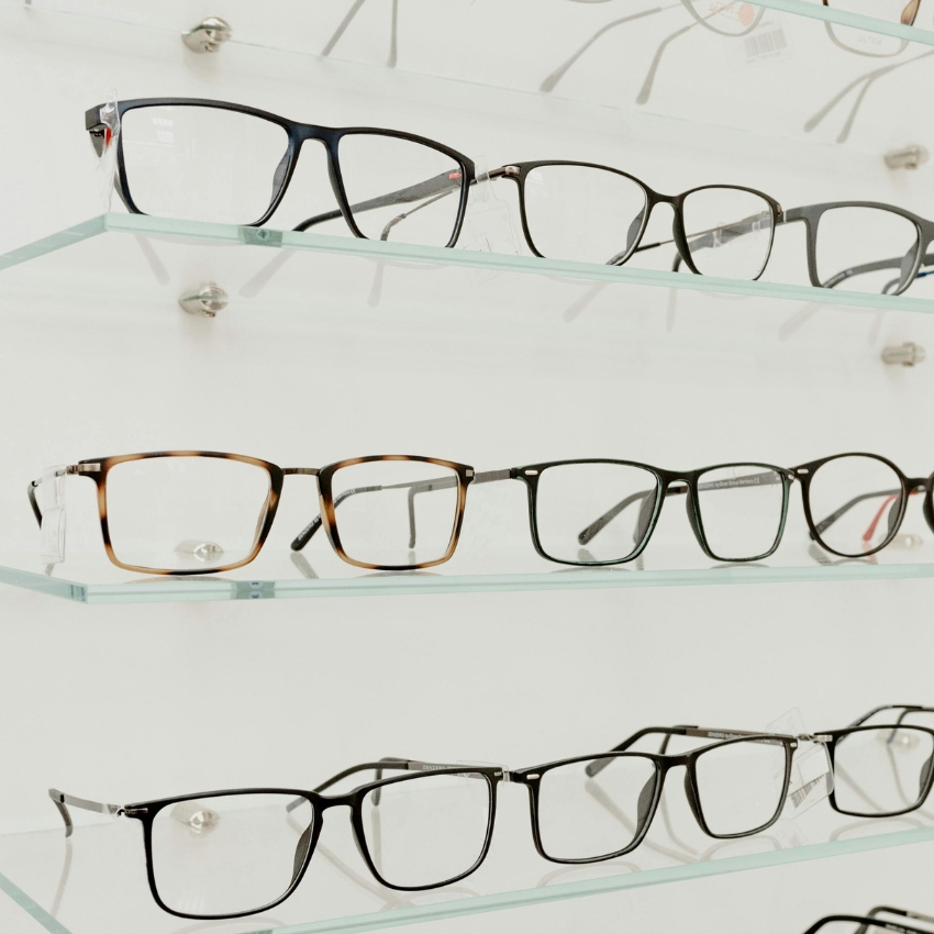 Various eyeglass frames displayed on glass shelves, including black, tortoiseshell, and metal designs.