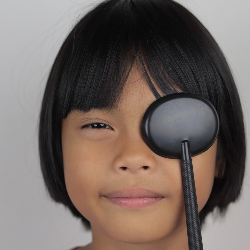 Child holding a black eye occluder over their right eye.