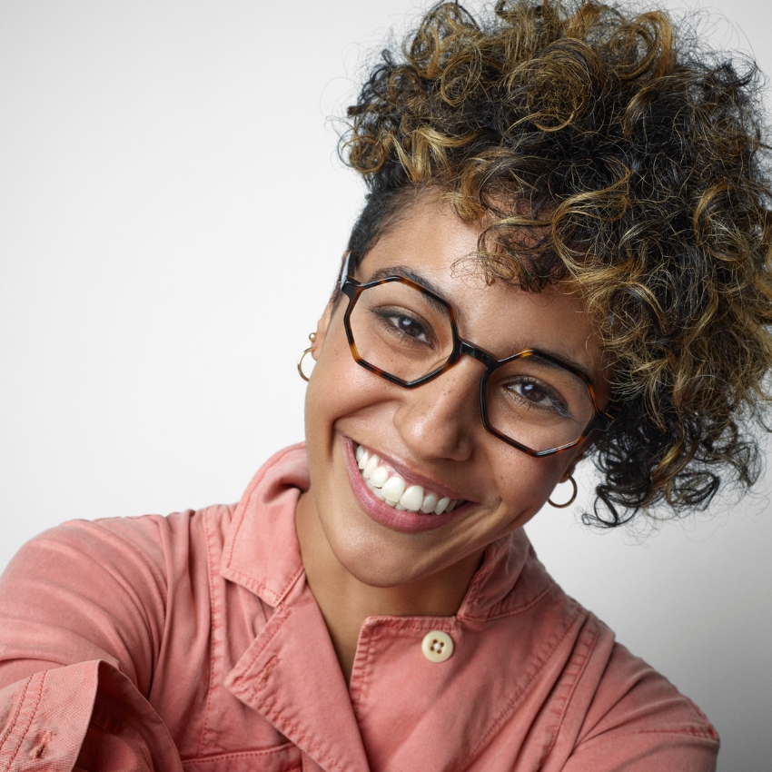 Tortoise shell geometric glasses worn with a pink jacket with a top button fastened.