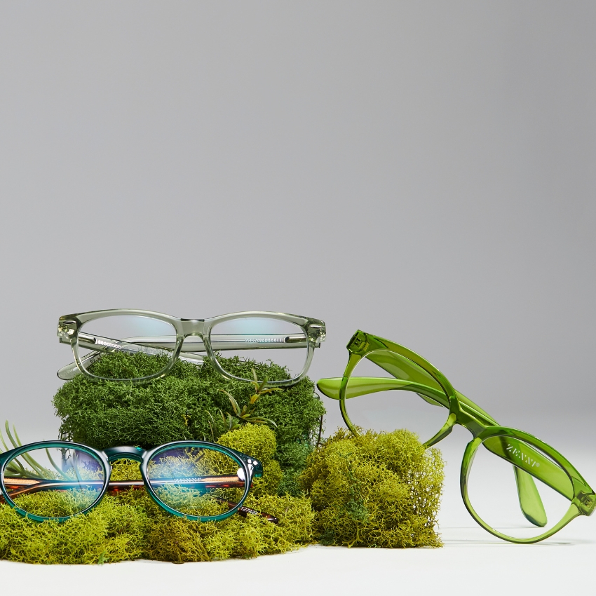 Three pairs of green and blue eyeglasses by Zenni, displayed on bright green moss.