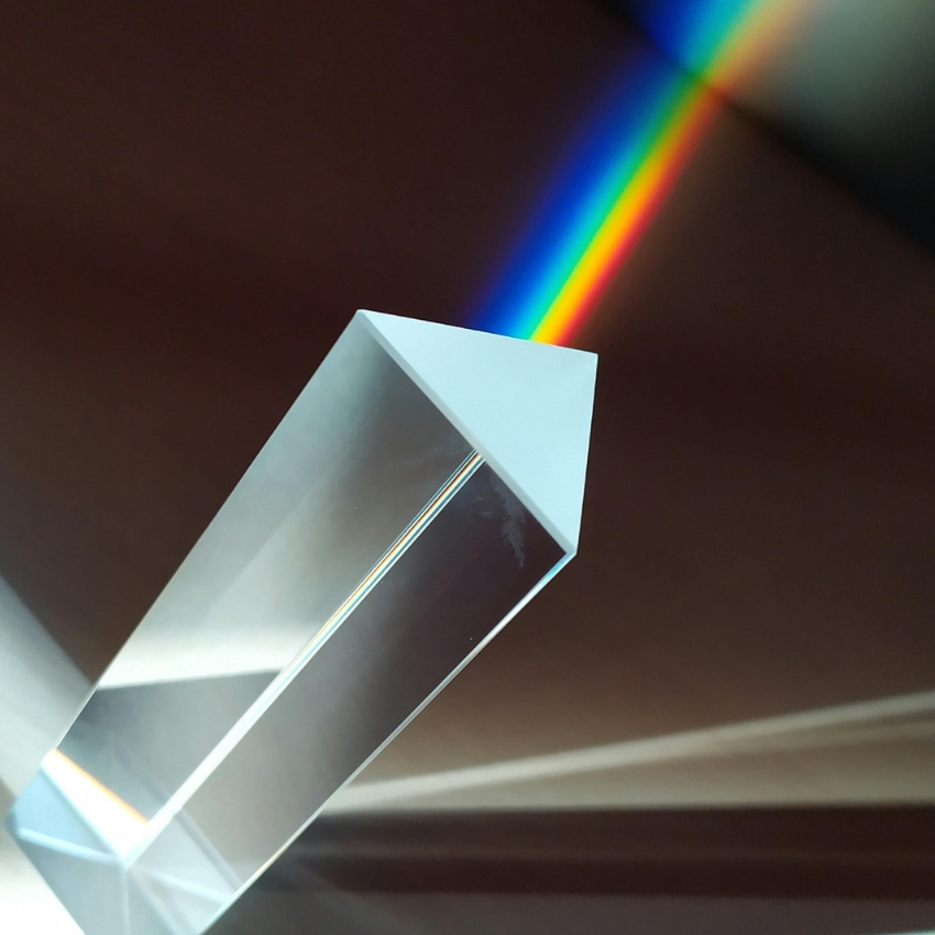 Triangular glass prism dispersing light into a vivid rainbow spectrum.