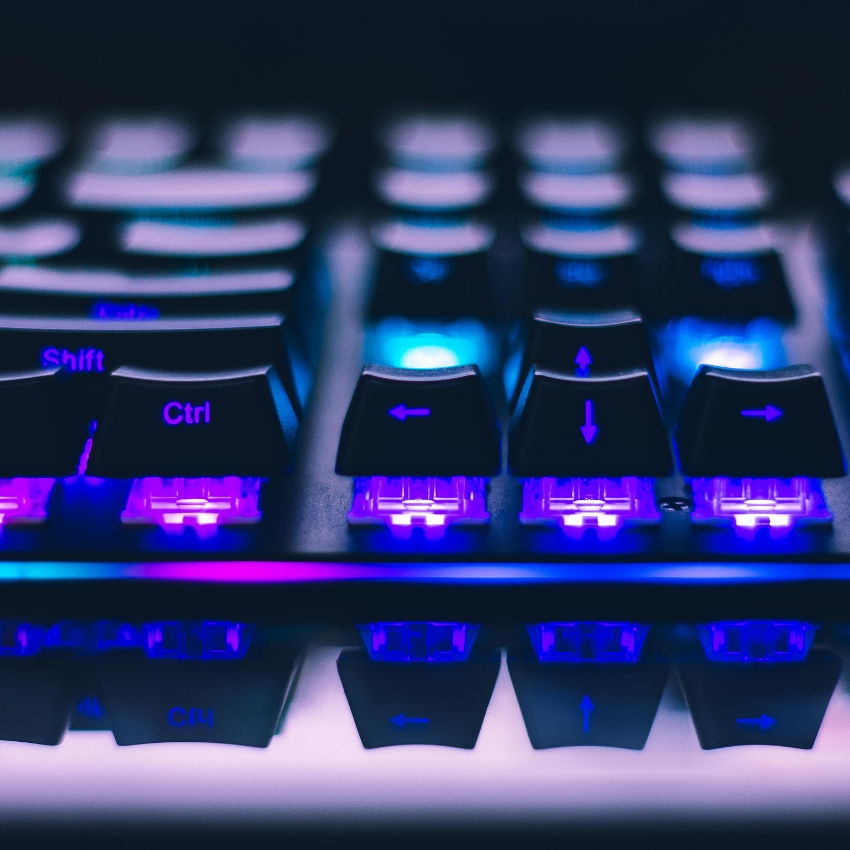 Mechanical keyboard with backlit keys showing Shift, Ctrl, and arrow keys illuminated in blue and purple.