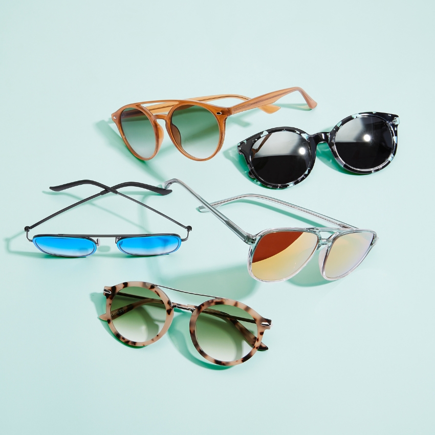 Five pairs of sunglasses on a light blue background: brown frames with green lenses, black frames with dark lenses, metal frames with blue lenses, silver frames with mirrored lenses, and tortoiseshell frames with brown lenses.