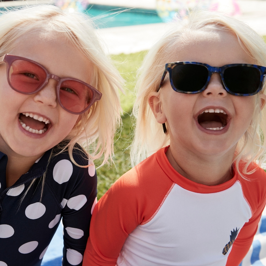 Kids wearing sunglasses and colorful swimsuits, one in polka dots and one in orange and white.