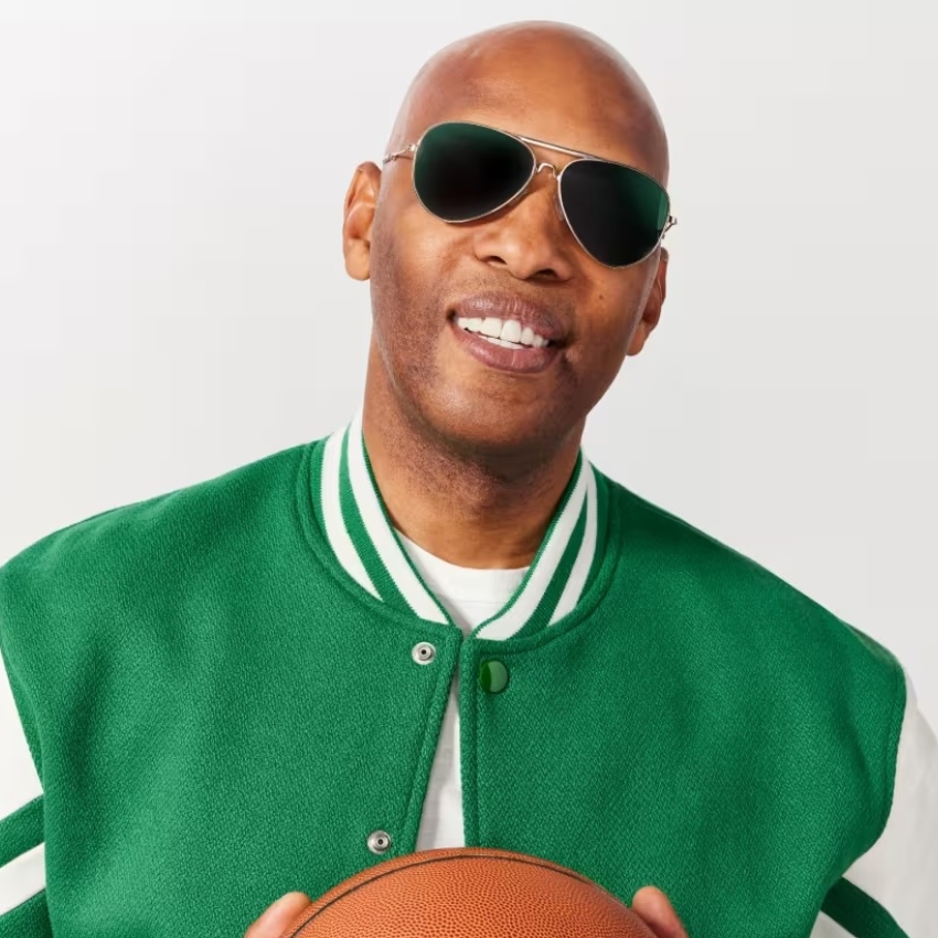 Man wearing sunglasses and a green varsity jacket, holding a basketball.