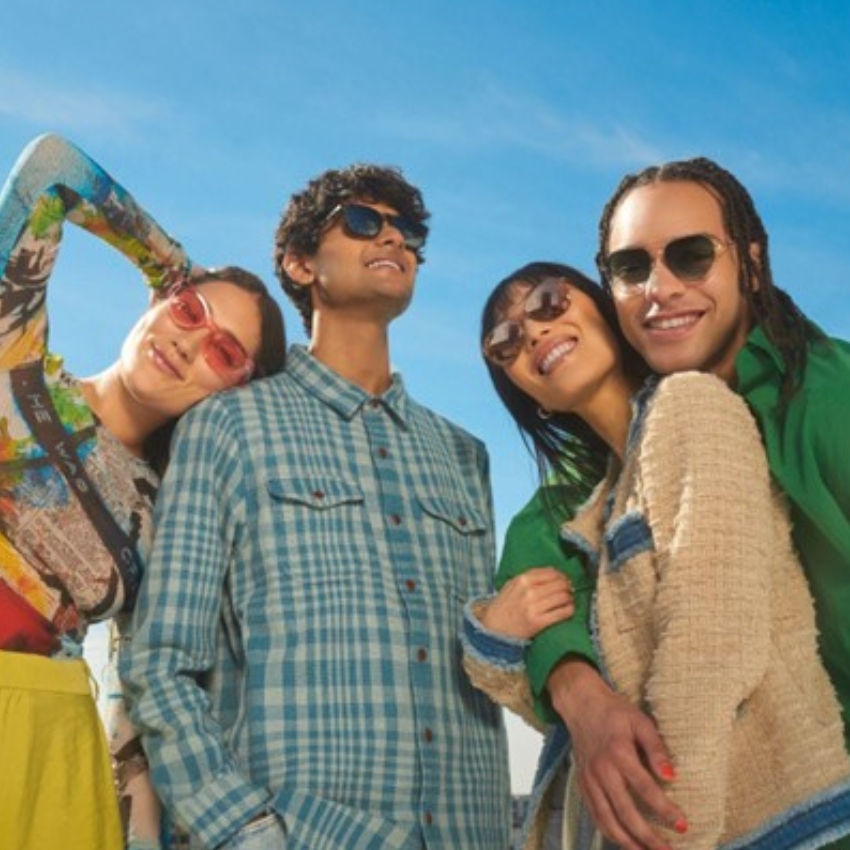 Group of four people wearing colorful clothing and sunglasses, smiling under a clear blue sky.