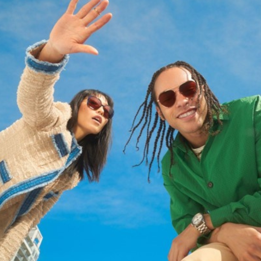 Two people wearing stylish sunglasses and colorful jackets against a backdrop of bright blue sky.