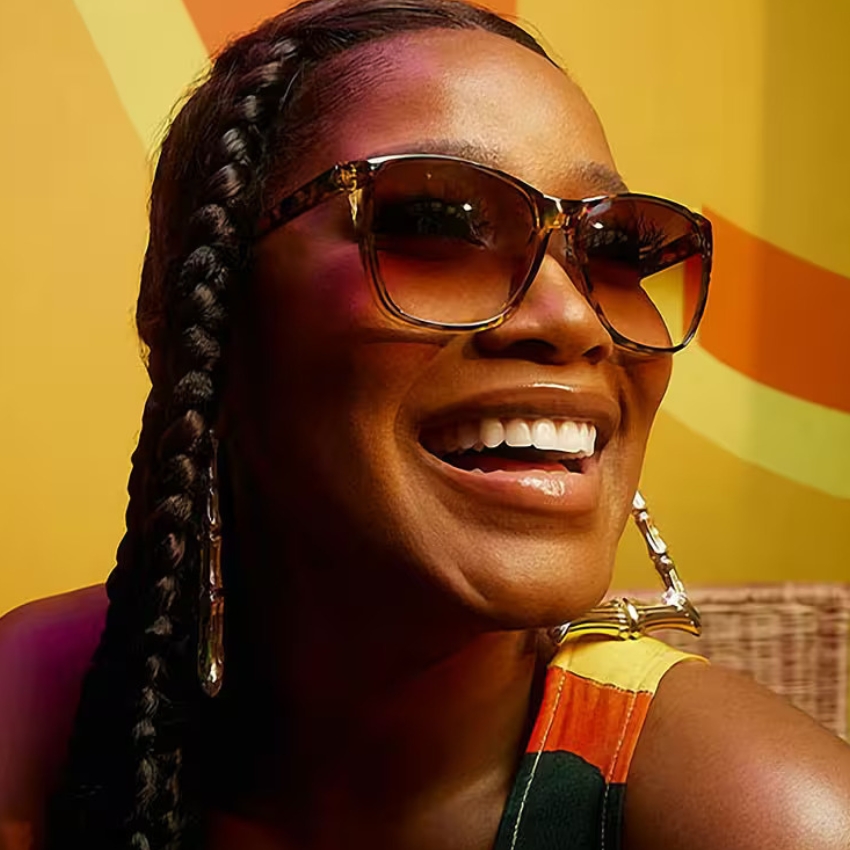 Woman wearing gold-rimmed sunglasses with gradient lenses, hoop earrings, and braided hairstyle.