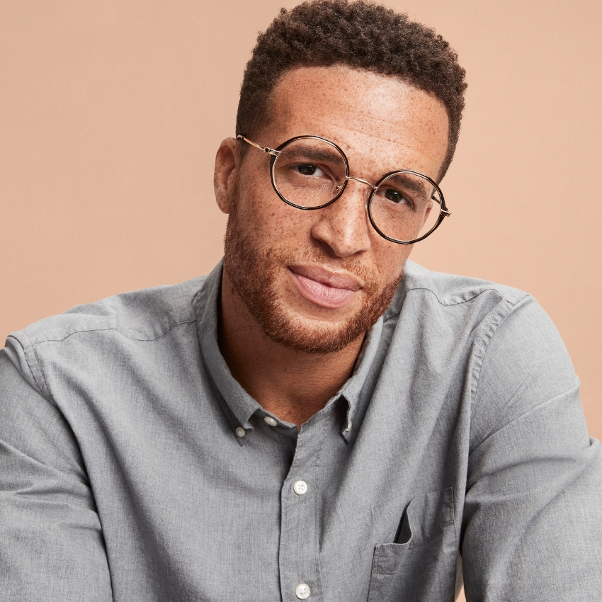 Man wearing round, gold-rimmed eyeglasses and a light gray button-down shirt.