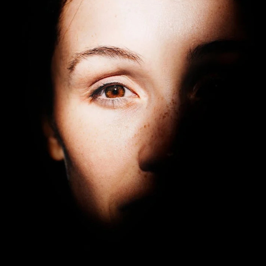 Close-up of a face half in shadow. One brown eye, eyebrow, and freckles are visible in the light.