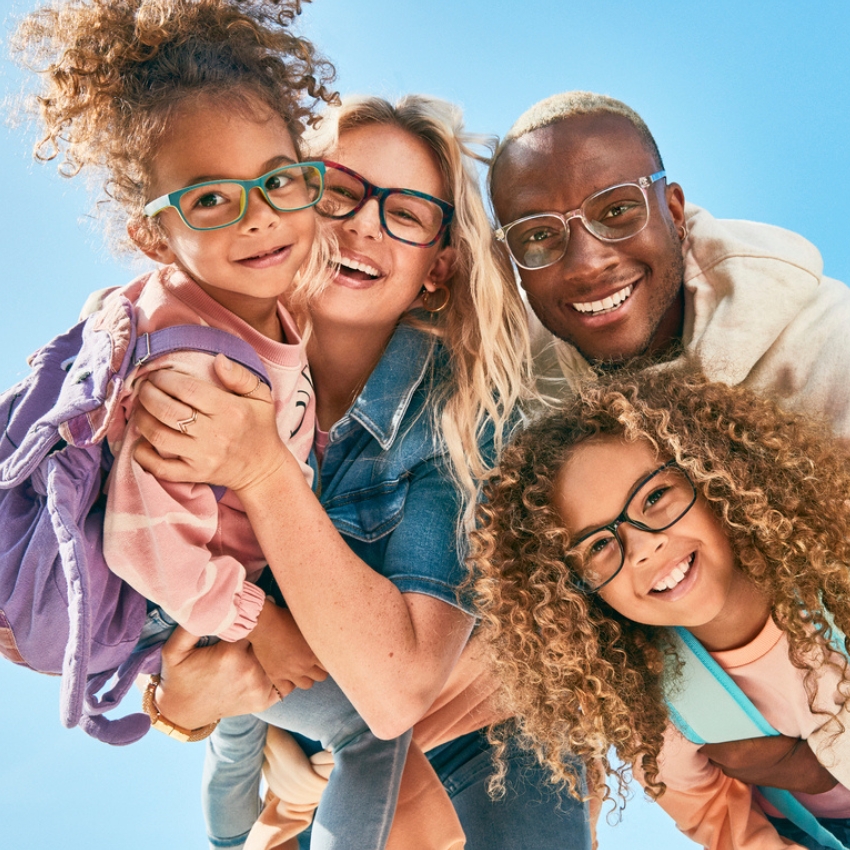 Family of four wearing colorful eyeglasses, with smiles and backpacks.