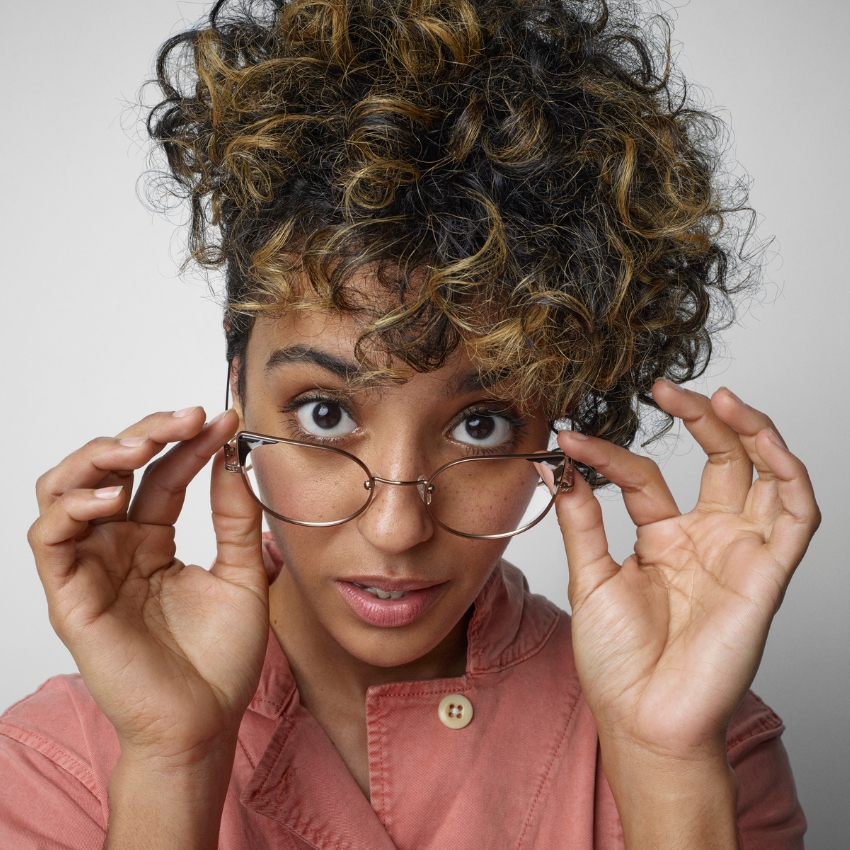 Woman adjusting oval eyeglasses with thin metallic frame.