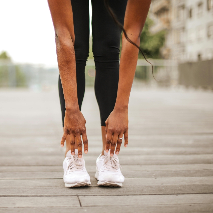 Person stretching while wearing white athletic shoes and black leggings.