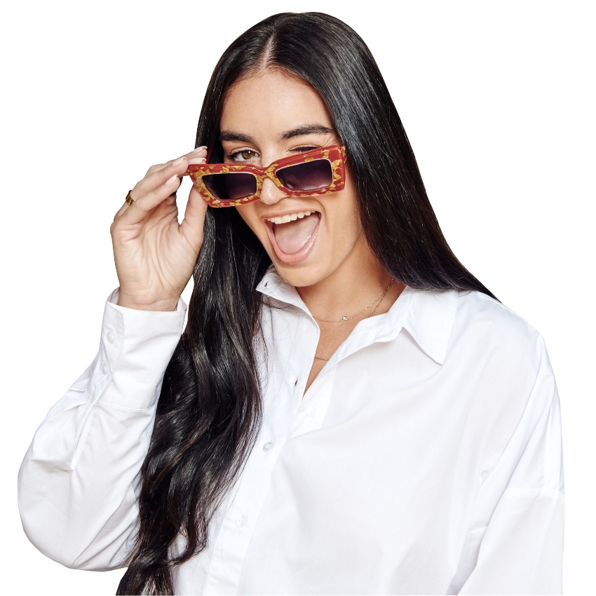 Woman wearing brown tortoiseshell rectangular sunglasses and a white button-up shirt, smiling with a wink.