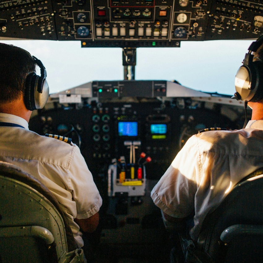 Two pilots in a cockpit, facing a control panel filled with various instruments and screens.