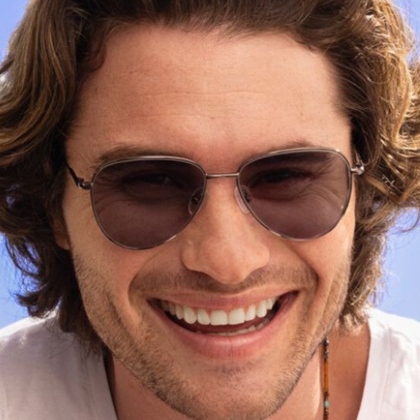 Man wearing aviator sunglasses, smiling with clear lenses and thin metal frames.