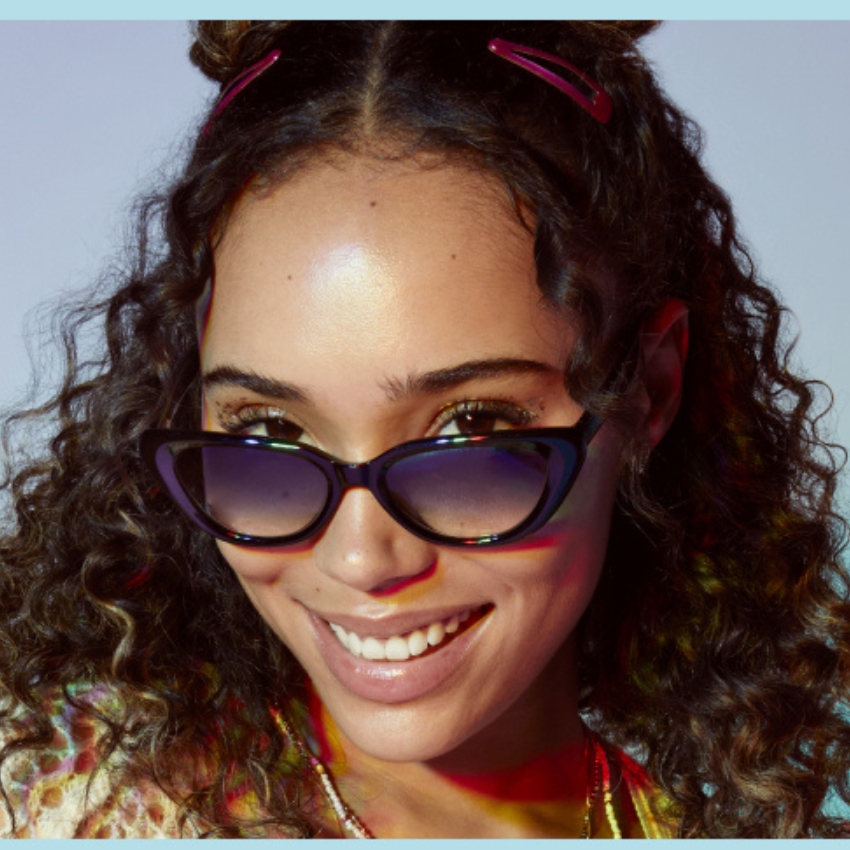 Woman wearing black cat-eye sunglasses with blue gradient lenses, smiling brightly.