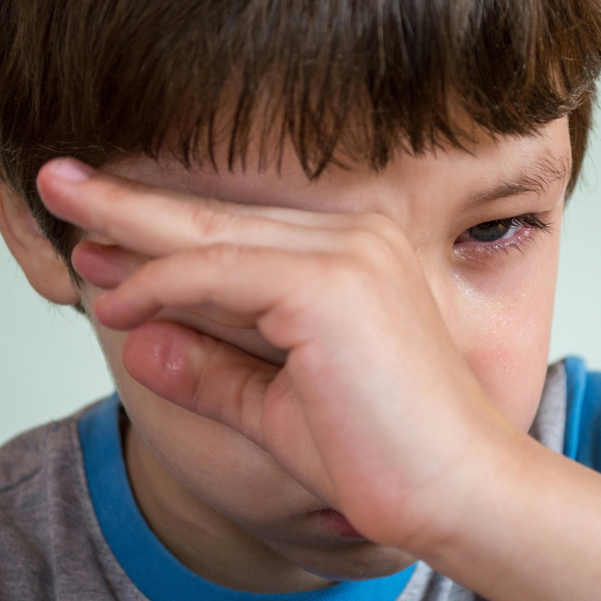 Child wiping tears from eyes with hand covering face.