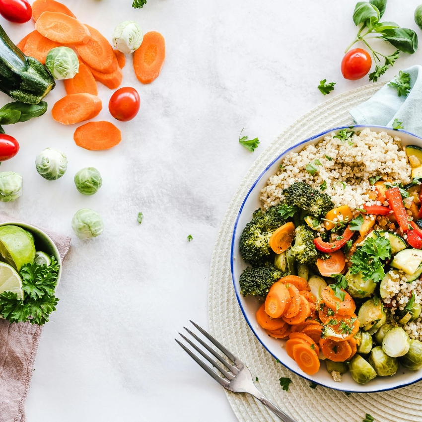 Bowl of quinoa with steamed broccoli, carrots, brussels sprouts, cherry tomatoes, bell peppers, and parsley.