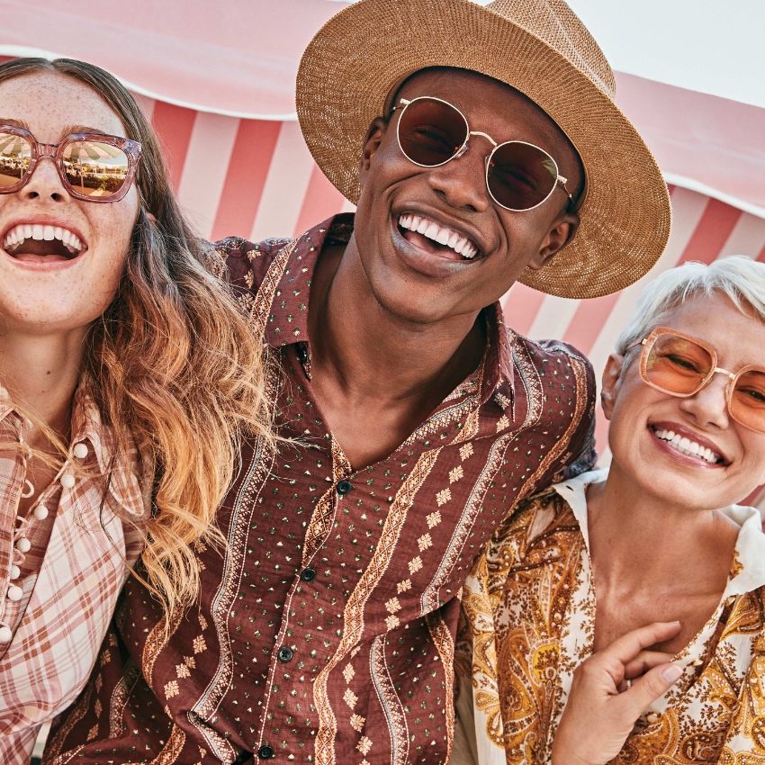 Three people wearing stylish sunglasses and patterned shirts, smiling and enjoying a sunny day.