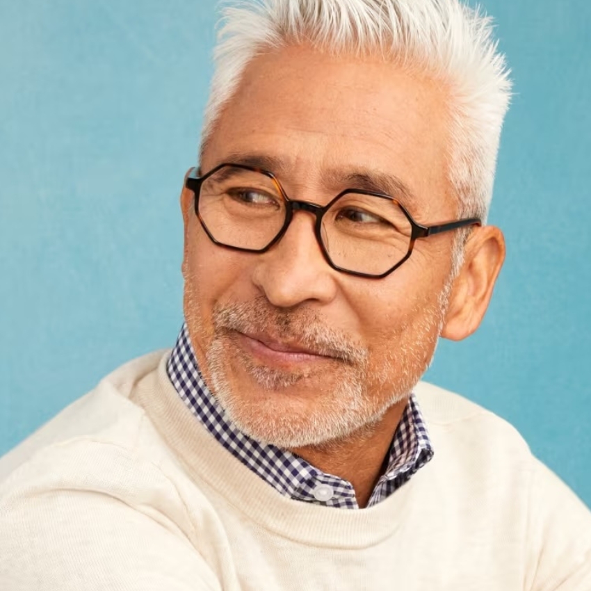 Man wearing a white sweater and black rectangular glasses, smiling and looking to the side.