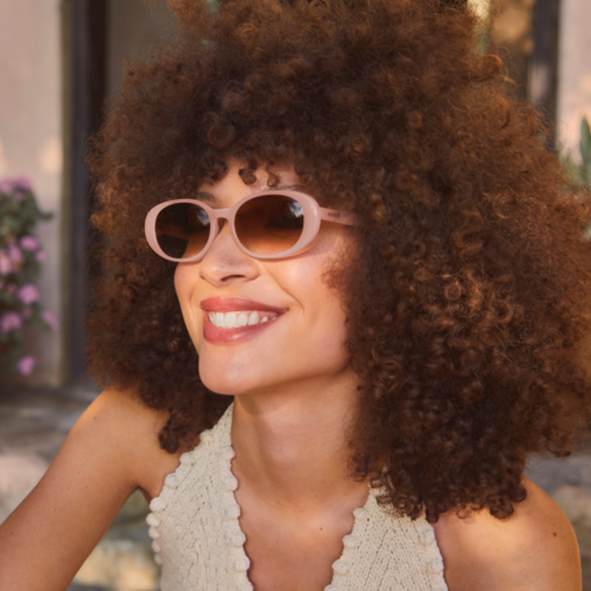 Woman wearing peach-colored, oval sunglasses with a cream knit top.