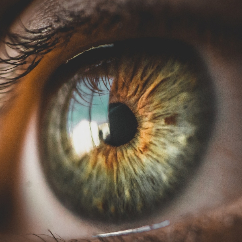 Close-up of a human eye with a green and brown iris and detailed reflection in the pupil.