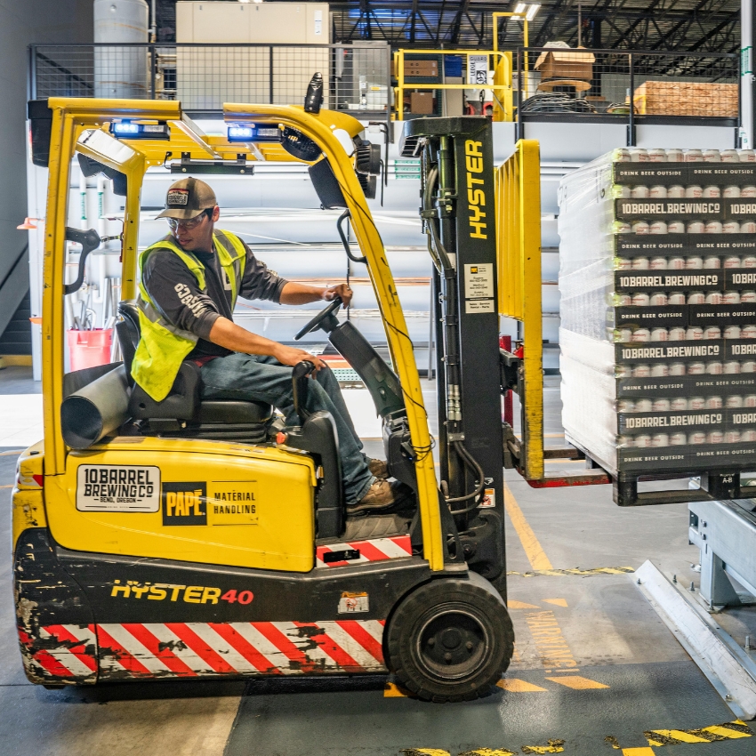 Yellow HYSTER 40 forklift operated by a worker, moving a pallet of 10 Barrel Brewing Co. boxes.