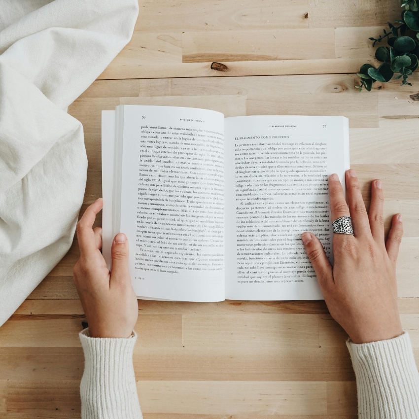 Book open to pages 76 and 77, being held by two hands wearing white sleeves.